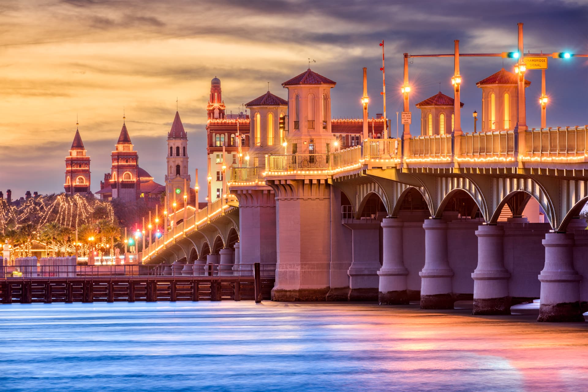 The Bridge of Lions lit up at sunset with historic spires beyond the water